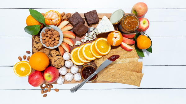 A flat lay of amaretti and chocolate chip cookies, bright slices of fresh apples and oranges, handmade crackers and nuts
