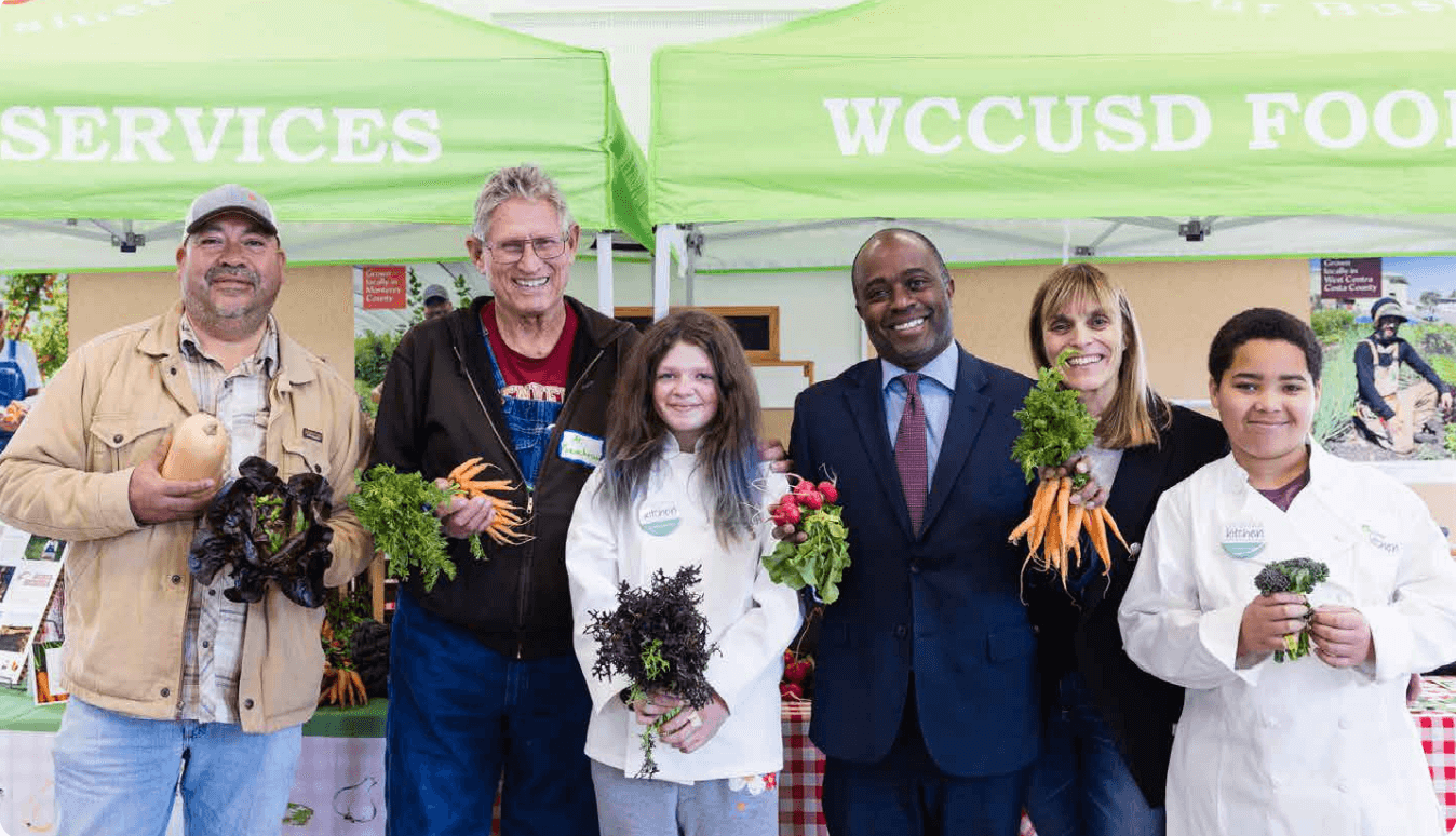 An image of five people smiling, including State Superintendent Tony Thurmond, Farmer Al, Farmer Javier, Judi Shils and Student Ambassadors at West Contra Costa Unified School District.