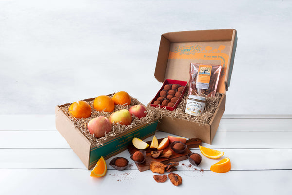 An attractive branded brown paper cardboard box filled with organges, apples, honey, and handmade truffles.