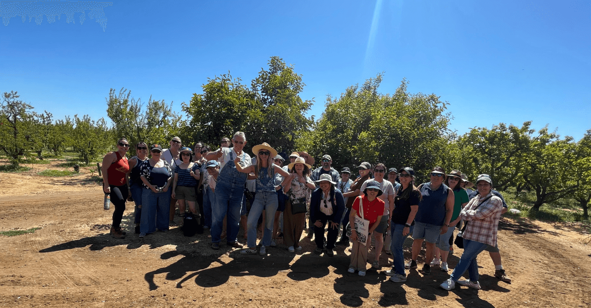 A group of people smiling for the camera outdoors, against a background of a tree orchard.