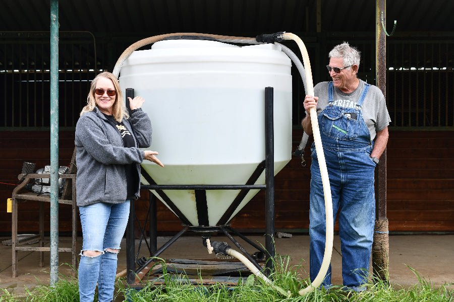 Farmer Al and Sarah, smiling and posing next to a large, 300-gallon vat of compost tea.