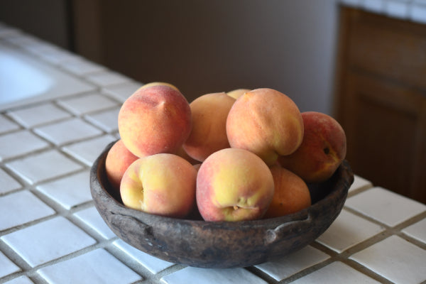 A close up image of a bowl of vibrant, fuzzy orange peaches, sitting on top of a white counter.