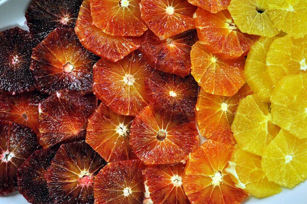 A close up image of several blood orange slices that vary in colors of vibrant yellows to deep burgandy.