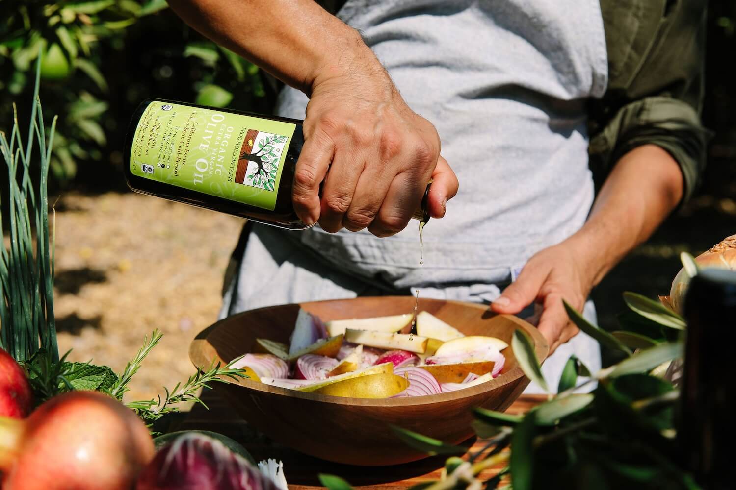 Olive oil being poured over a bowl of vegetables in an olive orchard